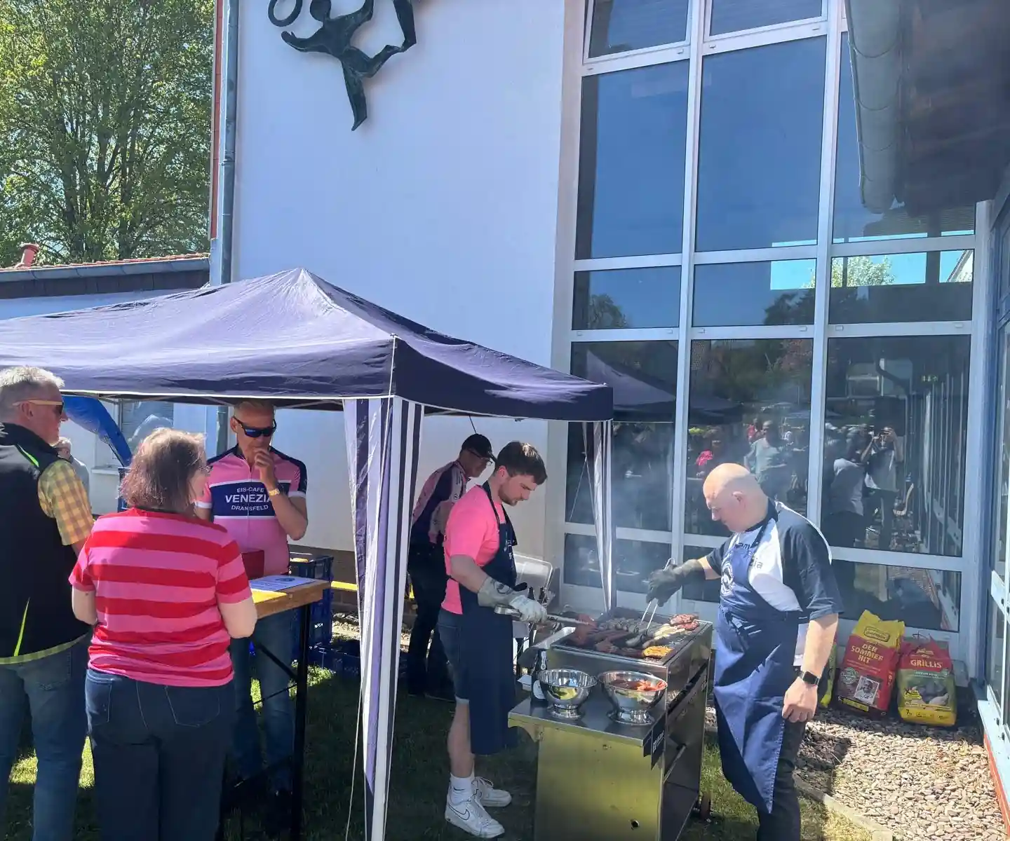 Am Grill neben der Stadthalle: Helfer wenden Würstchen, davor warten die Gäste