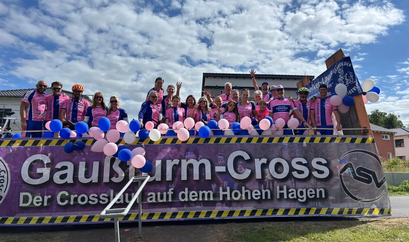 Die Vereinsgruppe in rosa-blauen Trikots auf dem Umzugswagen, davor ein Banner „Gaußturm-Cross — Der Crosslauf auf dem Hohen Hagen“