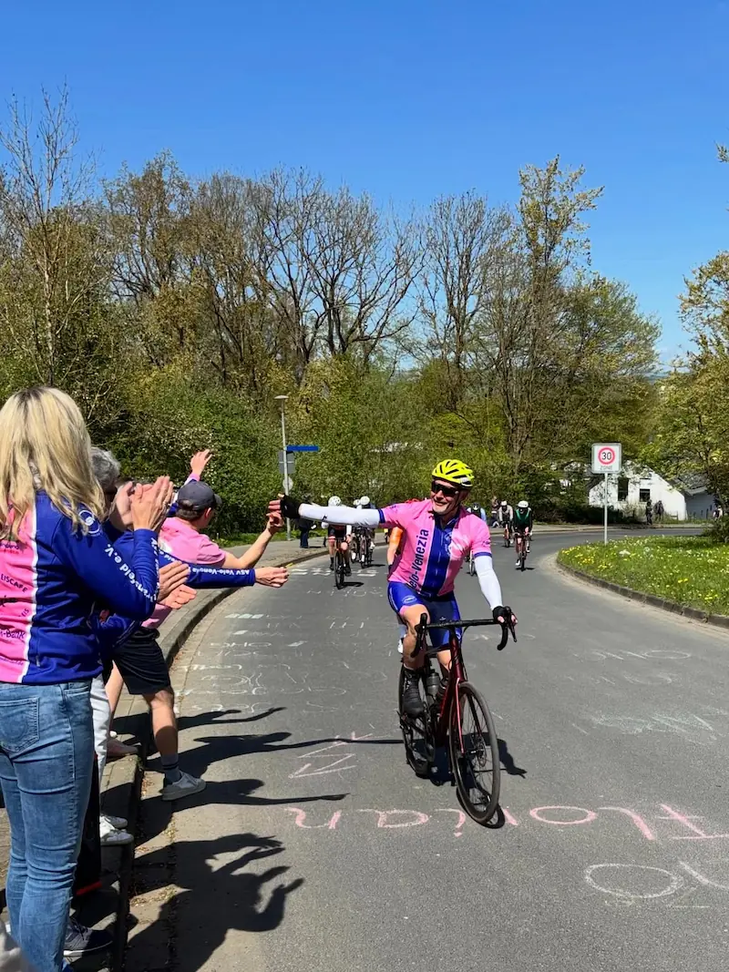 Radfahrer im rosa Velo-Venezia-Trikot wird von der Vereinsgruppe am Straßenrand angefeuert