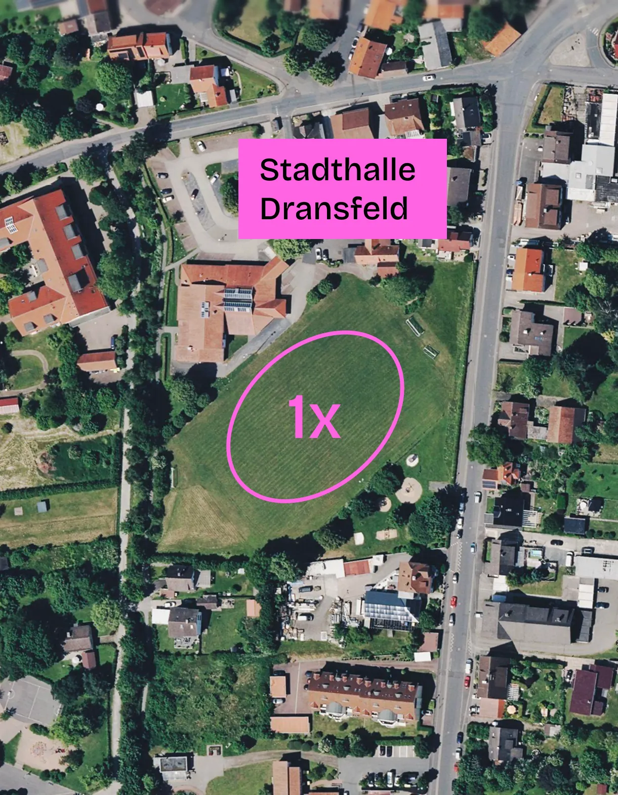 Satellitenbild des Sportplatzgeländes in Dransfeld mit einer pink eingezeichneten Runde auf dem Rasen, beschriftet mit „1x“. Ein pinkes Schild weist die Stadthalle Dransfeld aus.
